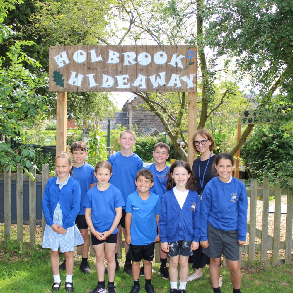 Students at Holbrook Primary School standing in front of a wooden sign that says 'Holbrook Hideaway'